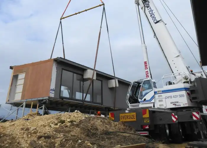 Tasbuilt Homes modular building section being lowered into place on site by a crane as part of a precision installation process.