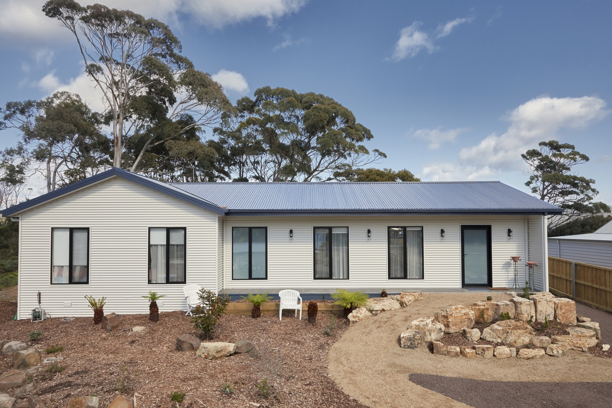 Exterior view of Tasbuilt Homes’ Cosy Coastal Retreat at White Beach, Tasmania, featuring an amended Clarendon design with light cladding, a semi-enclosed alfresco area, and large kitchen window capturing coastal views.