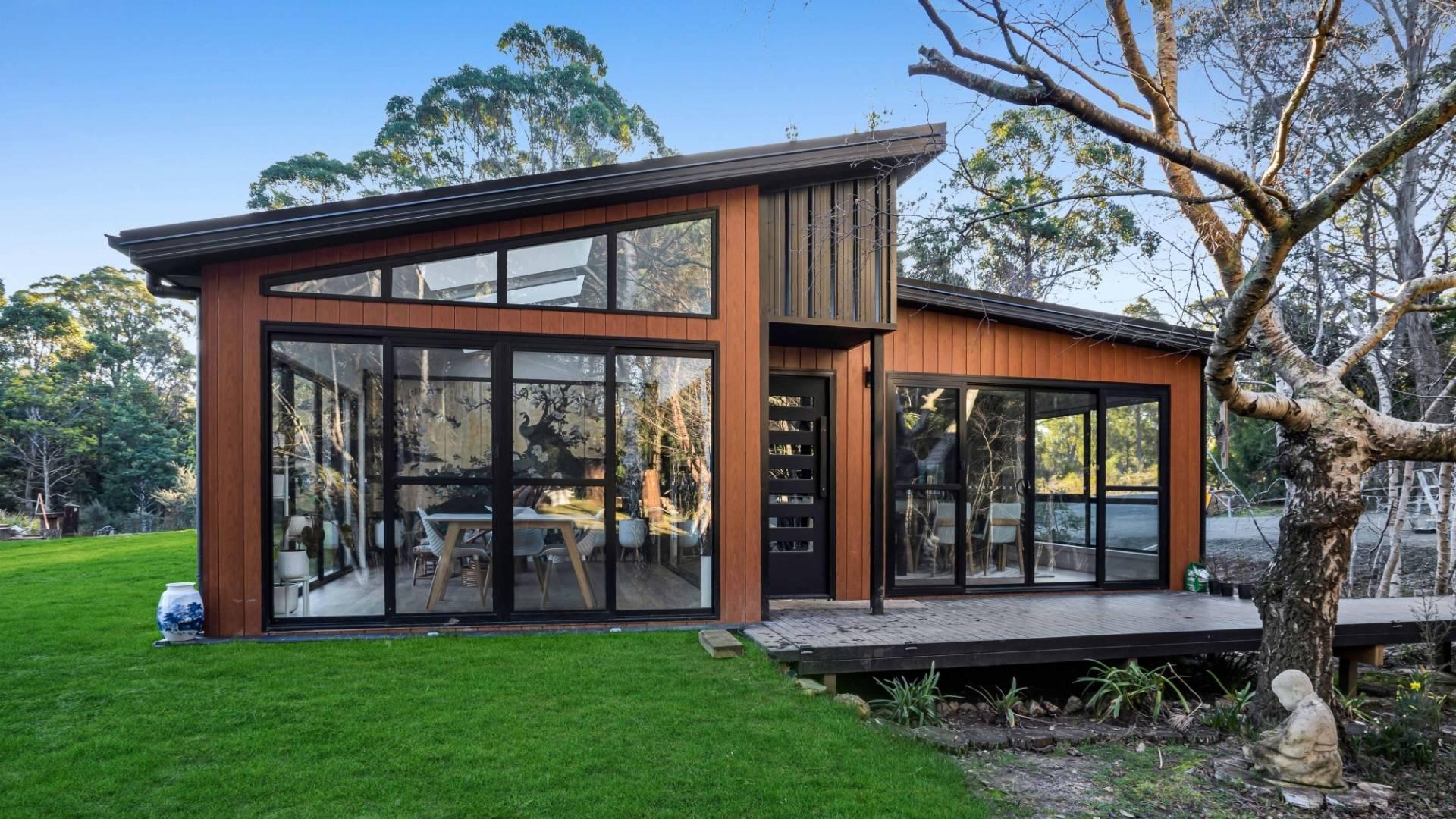 Exterior view of Tasbuilt Homes’ Luxurious Lakeside Retreat in Golden Valley, Tasmania, featuring a light-filled modular home with large windows overlooking the lake and surrounding mountains.