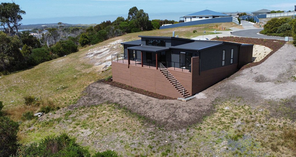 Exterior view of Tasbuilt Homes’ Earthy & Elegant Escape in Akaroa, Tasmania, showing a modern modular home with charcoal cladding, timber features, and elevated positioning overlooking the river.