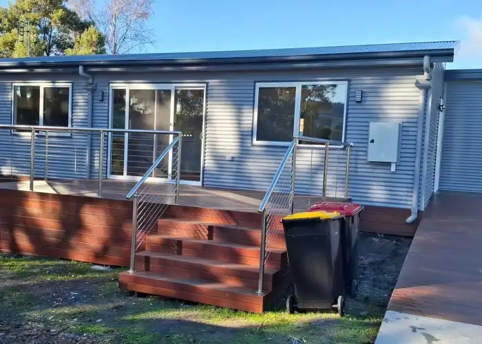 Exterior of a Tasbuilt home with grey corrugated iron cladding, deep timber decking, and silver balustrade.