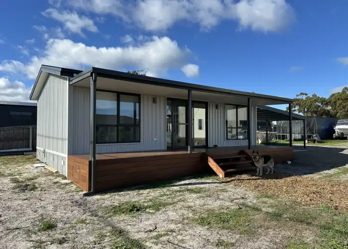 Exterior view of a Tasbuilt home with vertical silver cladding, dark gutters, and a timber deck.