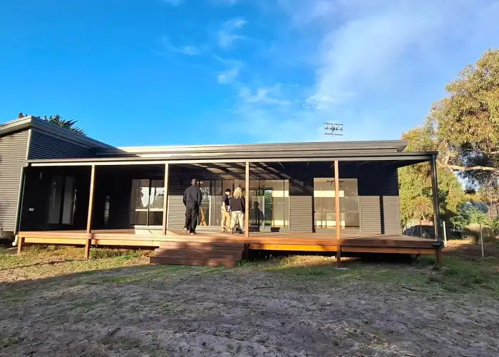 Tasbuilt clients receive their keys on the front deck of their new home, clad in black corrugated iron with timber decking.