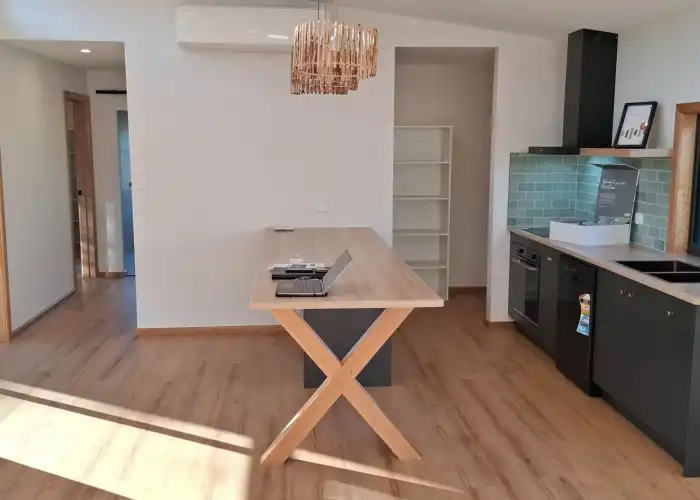 A stylish kitchen with white walls, dark cabinetry, charcoal fittings, and a green tiled splashback seen from a different angle.